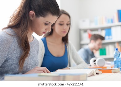 Girls studying together in the classroom, they are sitting at desk and reading a book, friendship and learning concept