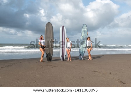 Girls surfers stand with boards on the beach.
