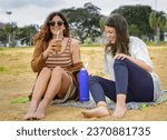 Girls talk while sitting on the beach drinking mate.