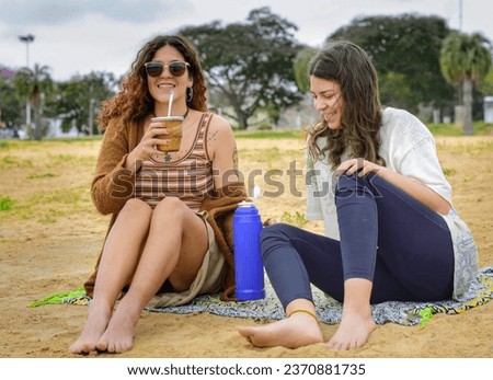 Girls talk while sitting on the beach drinking mate.