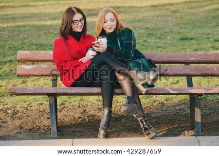 Girls walking around town on a sunny day with phones sitting on a bench and drink coffee