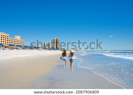 Girls walking and relaxing on the beach on the summer morning. Beautiful clear blue sky. Buildings and hotels in the background. Jacksonville, Florida, USA. Copy space.