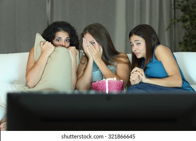 Girls watching a terror movie on tv sitting on a couch at home - Powered by Shutterstock