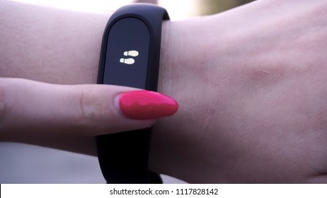 The Girls Wore A Fitness Bracelet. Girl Checks Pulse On Fitness Bracelet Or Activity Tracker Pedometer On Wrist, Sport, Technology And Healthy Lifestyle Concept, Close Up. Looks At The Pedometer