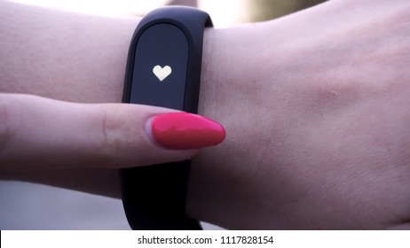 The girls wore a fitness bracelet. Girl checks pulse on fitness bracelet or activity tracker pedometer on wrist, sport, technology and healthy lifestyle concept, close up. Looks at the pedometer