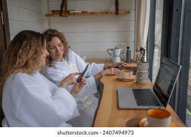 Girls working at laptops at same table distracted by conversation, chat, talk, sharing, show each other funny videos, photos, memes, interesting information, gossip during break from home remote study