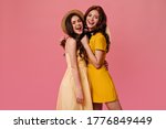 Girls in yellow dresses smiling on pink background. Lovely young women in summer light clothes cheerfully posing for camera