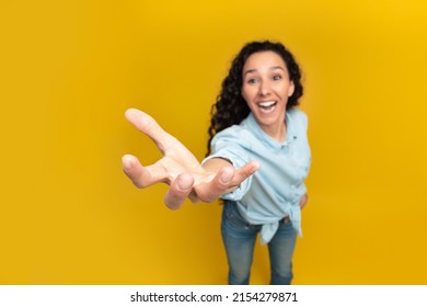 Give Me This. Young lady outstretching hand, trying to grab or hold something invisible on her open palm, asking for something, orange yellow wall, copy space, above top high angle overhead view