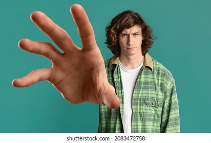 Give it to me. Young long-haired guy in casual outfit grabbing something on turquoise studio background, panorama, caucasian millennial man outstretching hand towards camera, creative image