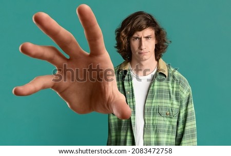 Give it to me. Young long-haired guy in casual outfit grabbing something on turquoise studio background, panorama, caucasian millennial man outstretching hand towards camera, creative image