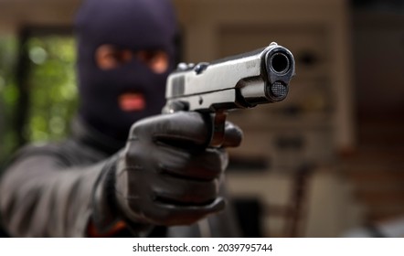 Give me your money otherwise you are dead. Blur robber with black balaclava aiming with pistol the victim. Hooded armed man thief killer in leather jacket holds gun in gloved hand. Weapon, crime.