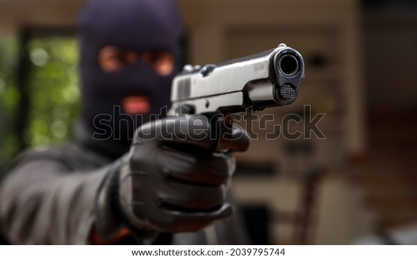 Give me your money otherwise you are dead. Blur\
robber with black balaclava aiming with pistol the victim. Hooded\
armed man thief killer in leather jacket holds gun in gloved hand.\
Weapon, crime.