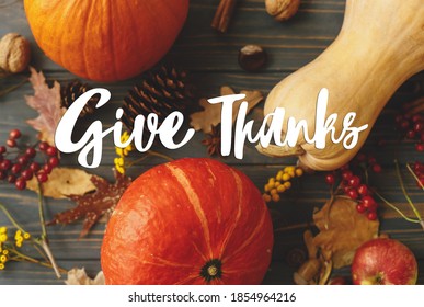 Give Thanks text handwritten on pumpkins, autumn leaves, apples, anise, cones, acorns and flowers on dark wood. Happy Thanksgiving greeting card. Seasons greetings