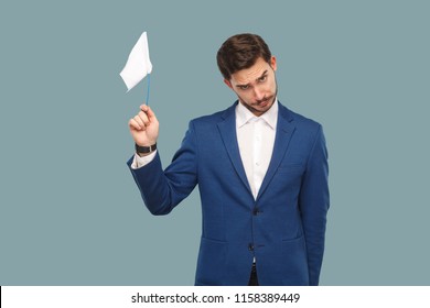 I Am Give Up. Sad Failure Businessman In Blue Jacket And White Shirt Standing And Holding White Flag And Looking At Camera With Sad Face. Indoor, Studio Shot Isolated On Light Blue Background.