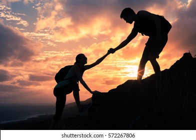 Giving A Helping Hand. Man Helping Female Climber Up A Mountain. 