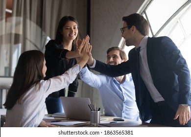 Giving high five. Excited international business team gathered on briefing in office uniting palms together celebrating common achievement, winning professional challenge, getting great work result