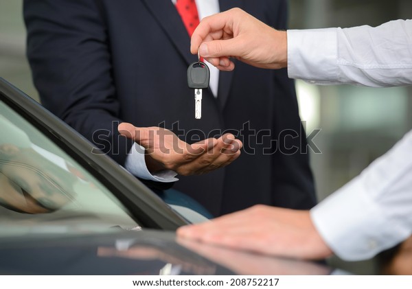 Giving a key of\
a brand new car. Handsome young classic car salesman giving a car\
key to the owner and\
smiling