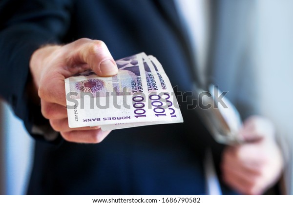 Giving money, Man holding norwegian currency in\
his hand. Front view.\
Norway.