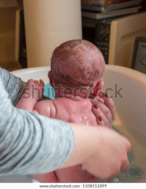 Female Child Sitting In Kitchen Sink Full Of Soapy Water Holding