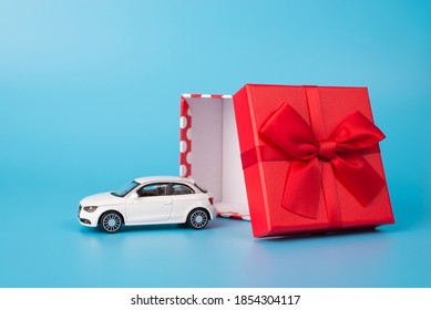 Giving and receiving gifts concept. Close up photo of white toy car beside open red giftbox with bow isolated on blue background