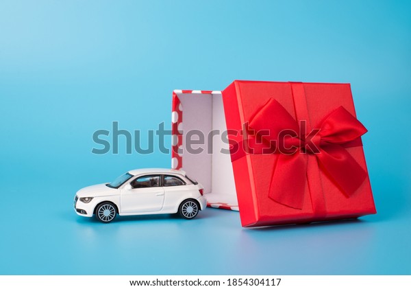 Giving and receiving gifts concept. Close up\
photo of white toy car beside open red giftbox with bow isolated on\
blue background
