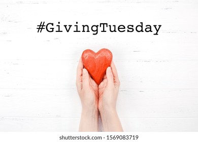 Giving Tuesday Is A Global Day Of Charitable Giving After Black Friday Shopping Day. Charity, Give Help, Donations And Support Concept With Text Message Sign And Red Wooden Heart In Woman Hands