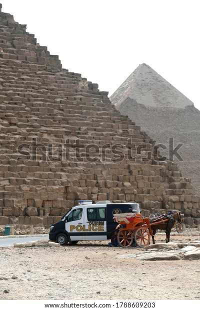 GIZA, EGYPT -\
MAR 11, 2020 - Police car and horse carriage base of the  Great\
pyramid of Cheops Khufu, Giza,\
Egypt