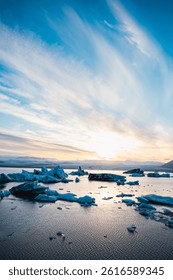 Glacial ice formations breaking apart in a pristine Icelandic lagoon, with golden light illuminating the snowy landscape.