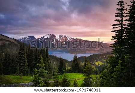 Glacial mountain Garibaldi lake at sunset. View of a mountain lake between fir trees. Mountain peaks above the lake lit by sunset rays. Garibaldi Provincial Park. Canada