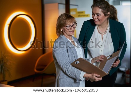 Glad assistant smiling while manager looking through paper folder