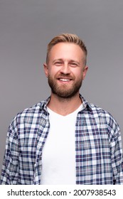 Glad bearded man with blond hair and in checkered shirt smiling and looking at camera against gray background - Shutterstock ID 2007938543