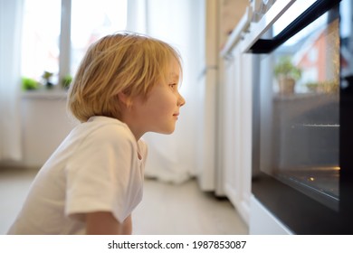 Glad boy sitting on the floor near kitchen stove and waiting for a pie or other baked goods to be prepared. Children love food prepared by their mother. Domestic cuisine. Healthy food for kids.