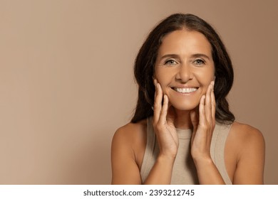 Glad caucasian old woman with natural makeup touch hands to soft face, enjoy skin care, isolated on beige studio background. Beauty care, anti-wrinkle treatment and spa procedures - Powered by Shutterstock