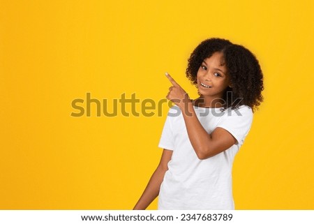Glad cheerful adolescent african american girl in white t-shirt, point finger to empty space, isolated on orange background, studio. Recommendation, advice for study, school education, ad and offer