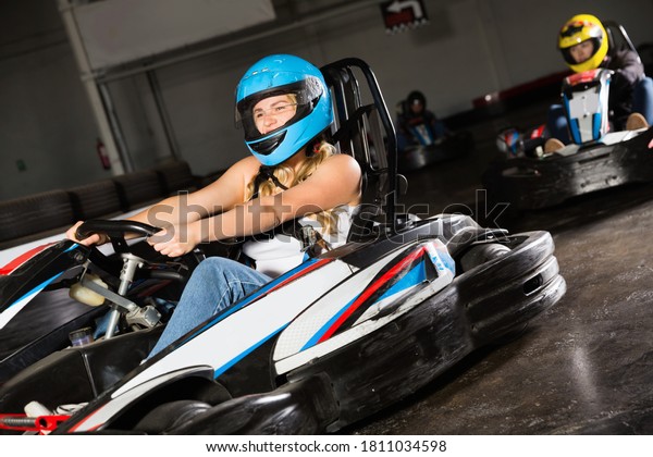 Glad cheerful positive girl and her friends\
competing on racing cars at kart\
circuit