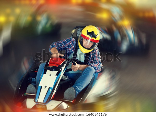 Glad cheerful\
positive smiling male in helmet  and other people driving cars for\
karting in sport club\
indoor