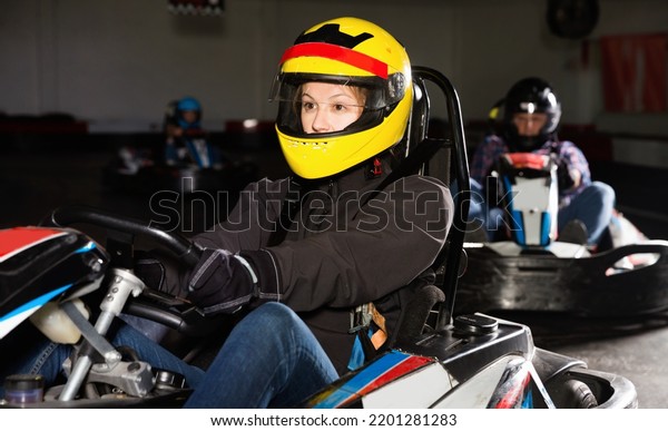 Glad cheerful smiling girl and her friends\
competing on racing cars at kart\
circuit