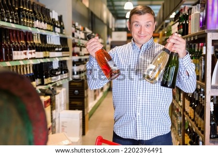 Glad cheerful smiling male customer choosing wine in supermarket .