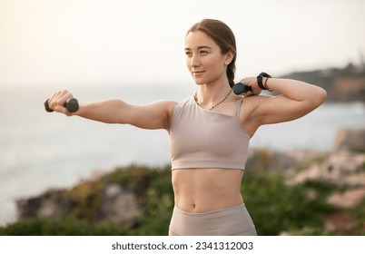 Glad confident strong millennial caucasian woman athlete in sportswear doing arm exercises with dumbbells, enjoy workout, body care alone at sea beach. Sports, fitness outdoor - Powered by Shutterstock