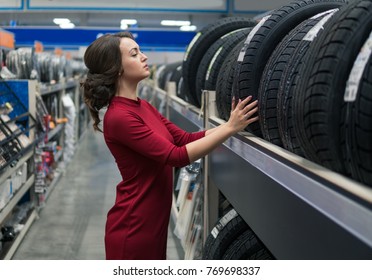 Glad Female Customer Taking New Tires In The Supermarket For Buying. She Looks Happy. Big Shopping Mall With Car Goods.