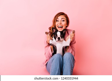 Glad Girl In Jeans Playing With Funny Little Dog. Indoor Portrait Of Excited Ginger Lady With Curly Hairstyle Spending Time With Her Puppy.