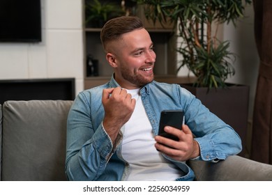 Glad handsome businessman wearing casual wear surfing net on smartphone sitting on sofa in background. Concept of smiling business person, pleased man, information, internet communication - Shutterstock ID 2256034959