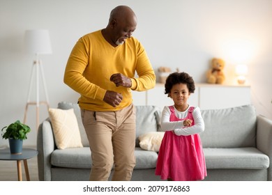 Glad Happy African American Small Girl And Old Man Dancing, Have Fun In Living Room Interior. Party At Home, Granddaughter And Grandfather Enjoy Spare Time, Grandpa Visit. Family And Relationship