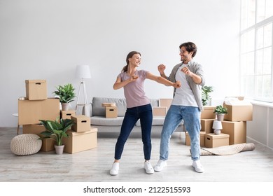 Glad Happy European Millennial Guy And Female Have Fun Dancing Together In Room Interior Among Boxes With Belongings. Rent Flat, Couple Enjoys Moving Day, Buy Home, Mortgage And Loan, Full Length