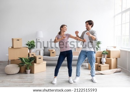 Glad happy european millennial guy and female have fun dancing together in room interior among boxes with belongings. Rent flat, couple enjoys moving day, buy home, mortgage and loan, full length