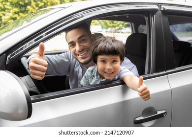 Glad Happy Millennial Arab Guy Teaches Little Boy To Drive Car, Dad And Son Show Thumbs Up In Open Window, In Summer, Outdoor. Family Enjoy Time Together At Weekend, Driving Lesson And Great Result