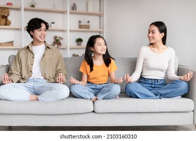 Glad Happy Pretty Teen Korean Girl, Millennial Mother And Father Sits In Lotus Position, Practice Yoga On Sofa In Room Interior. Meditation, Rest, Sports At Home Together, Vitality And Health Care