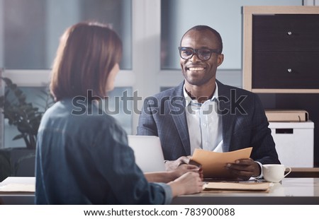 Glad to hear it. Portrait of optimistic young qualified manager is looking at his colleague female with smile while sitting at table and having pleasant communication. Back view of woman