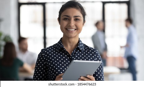 Glad To Help You! Portrait Of Smiling Confident Indian Female Insurance Broker Bank Manager Hr Assistant Standing In Open Space Office Holding Digital Tablet Looking At Camera Ready To Assist Client