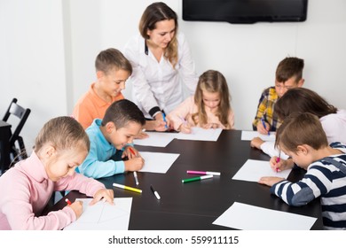 Glad Little Children With Teacher Drawing In Classroom On The Lesson